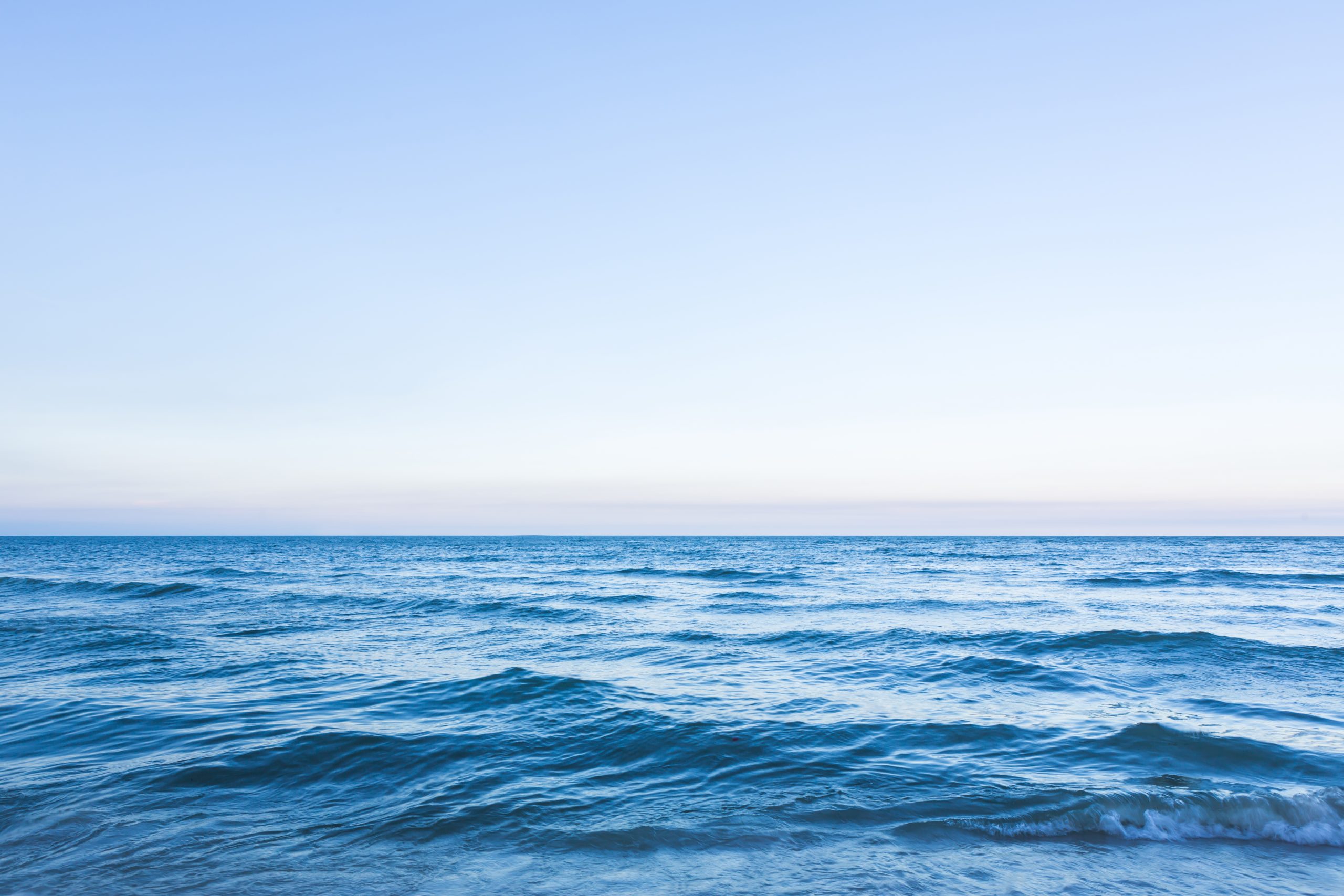 Image of the sea's calm surface. The sea is blue. The sky is cloudless.